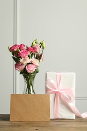 Photo of Happy Mother's Day. Gift box, blank card and bouquet of beautiful flowers in vase on wooden table near white wall