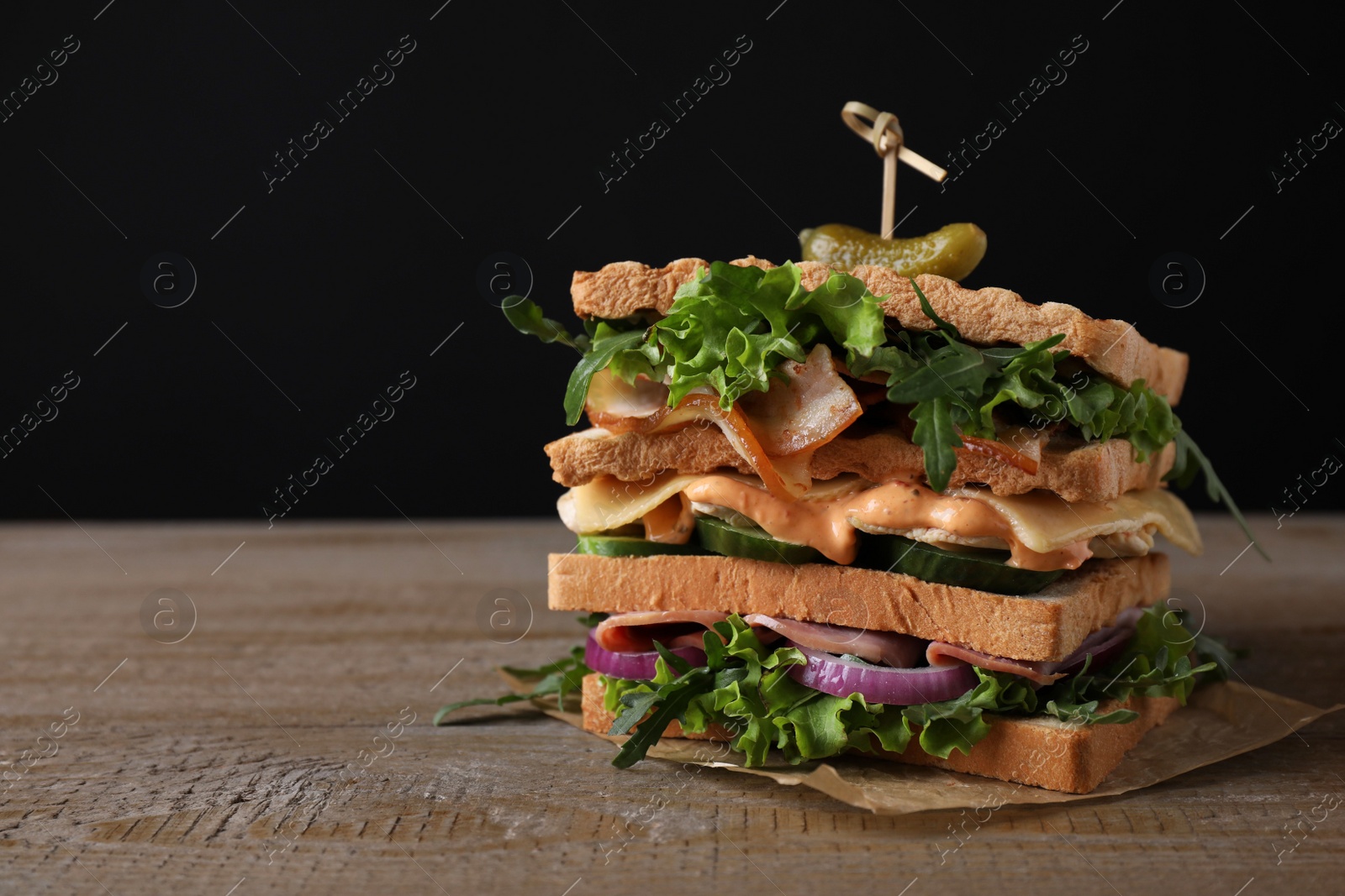 Photo of Tasty sandwich with chicken, ham and bacon on wooden table against black background. Space for text