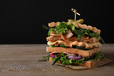 Photo of Tasty sandwich with chicken, ham and bacon on wooden table against black background. Space for text