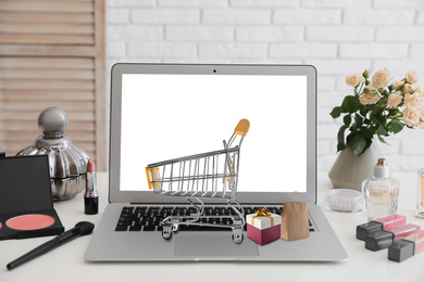 Image of Online shopping. Modern laptop with small cart, box and bag on table