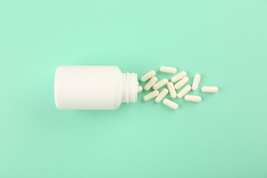 Bottle and vitamin capsules on turquoise background, top view