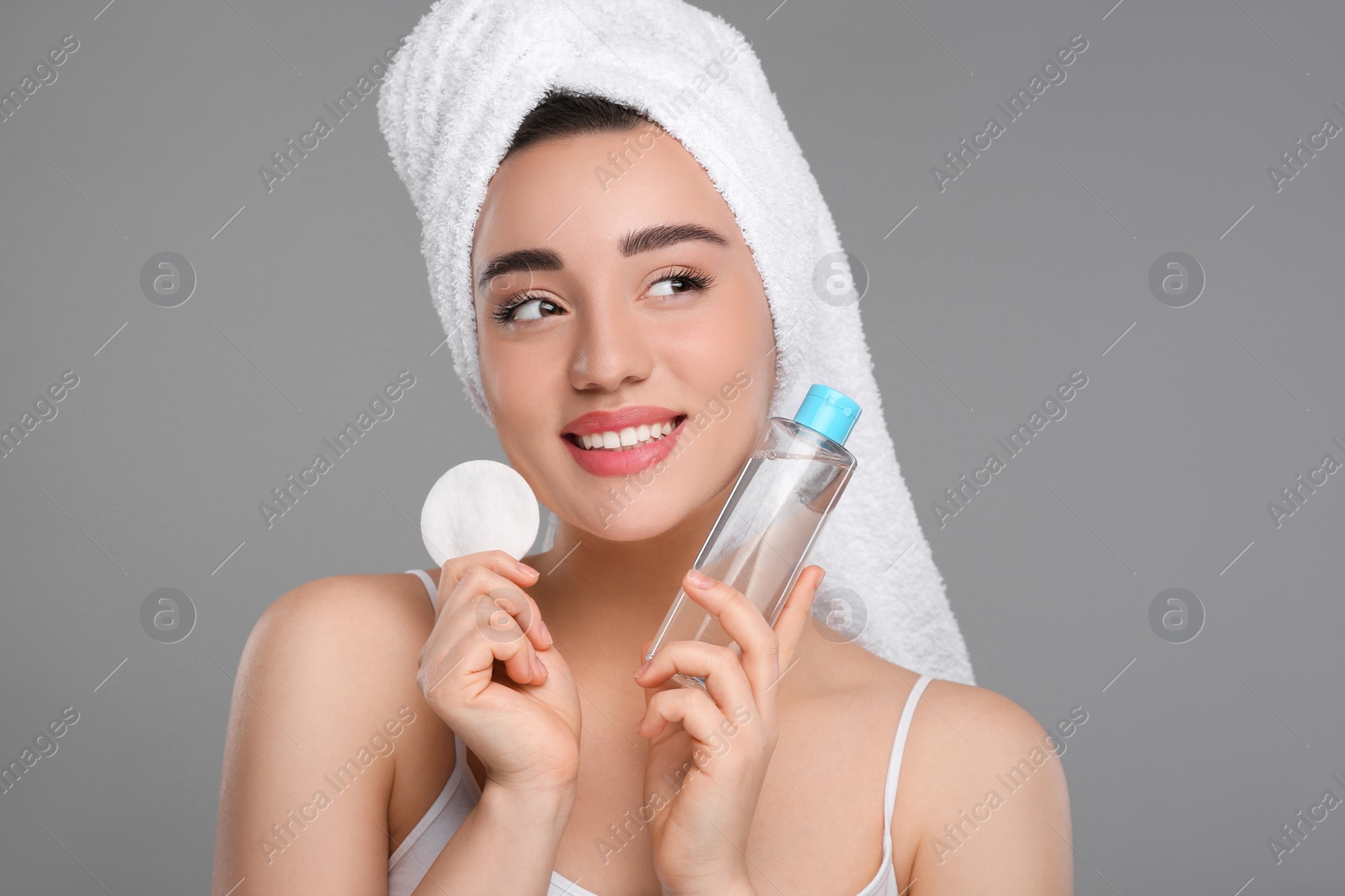 Photo of Beautiful woman in terry towel with makeup remover and cotton pad on gray background