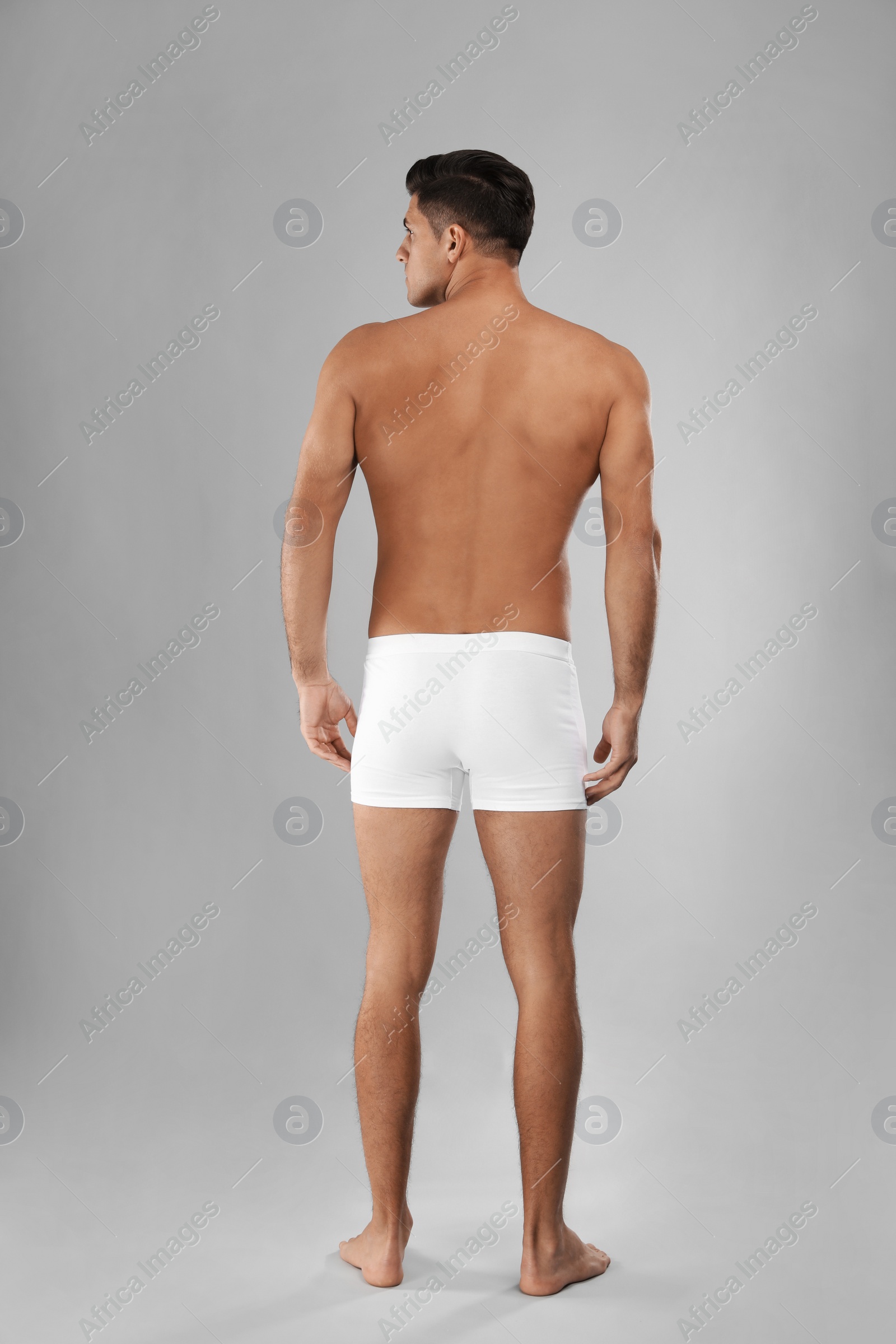 Photo of Handsome man in white underwear on light grey background, back view