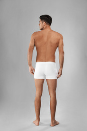 Handsome man in white underwear on light grey background, back view