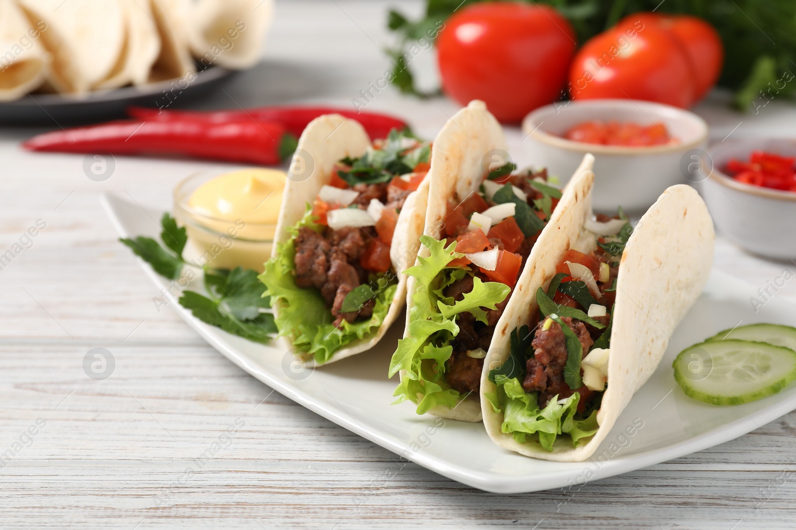 Photo of Delicious tacos with meat and vegetables on wooden table, closeup