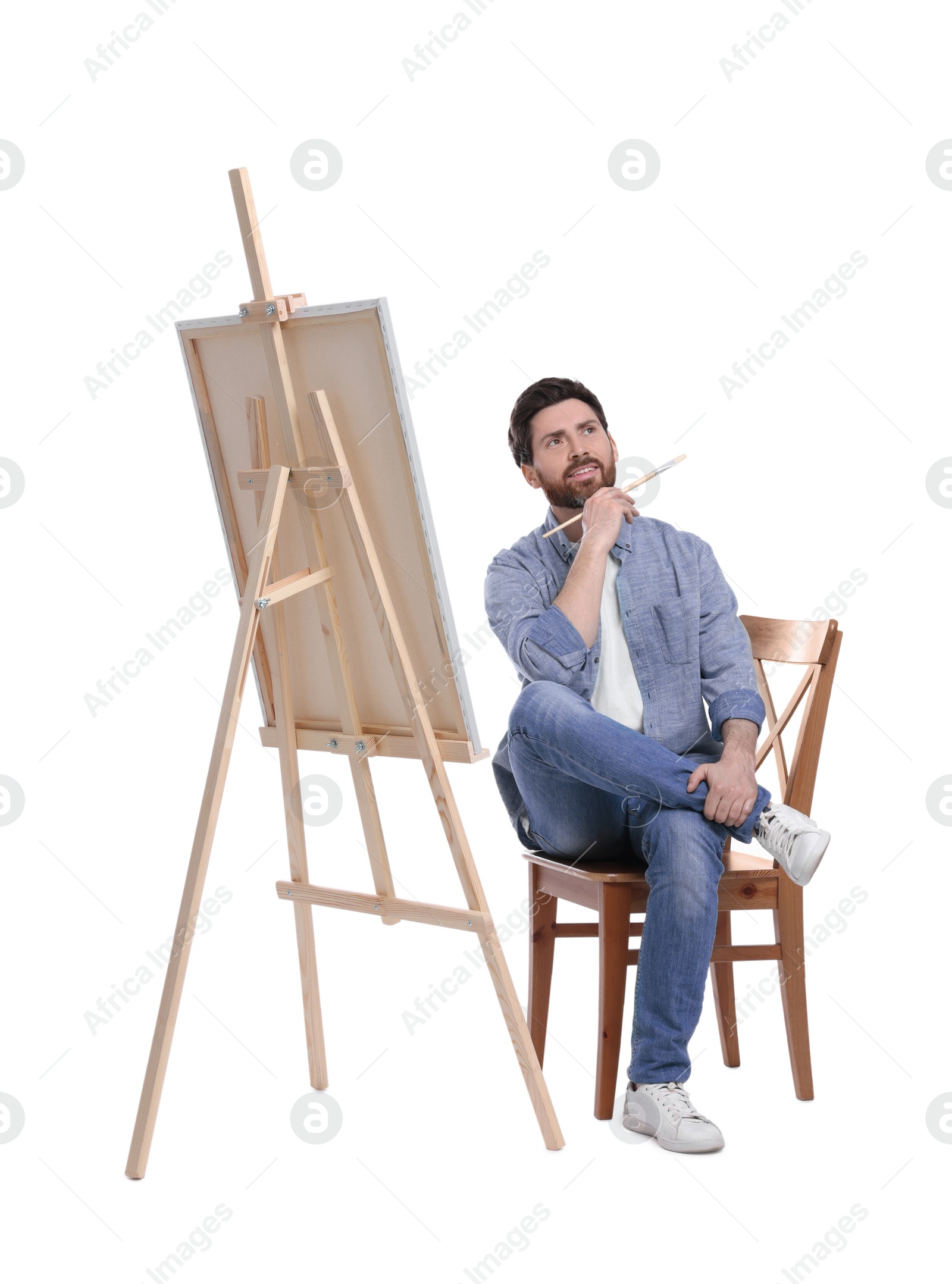 Photo of Man with brush painting against white background. Using easel to hold canvas