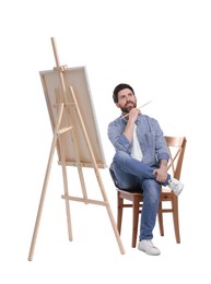 Man with brush painting against white background. Using easel to hold canvas