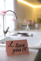 Photo of Note with handwritten text I Love You on countertop in kitchen. Romantic message