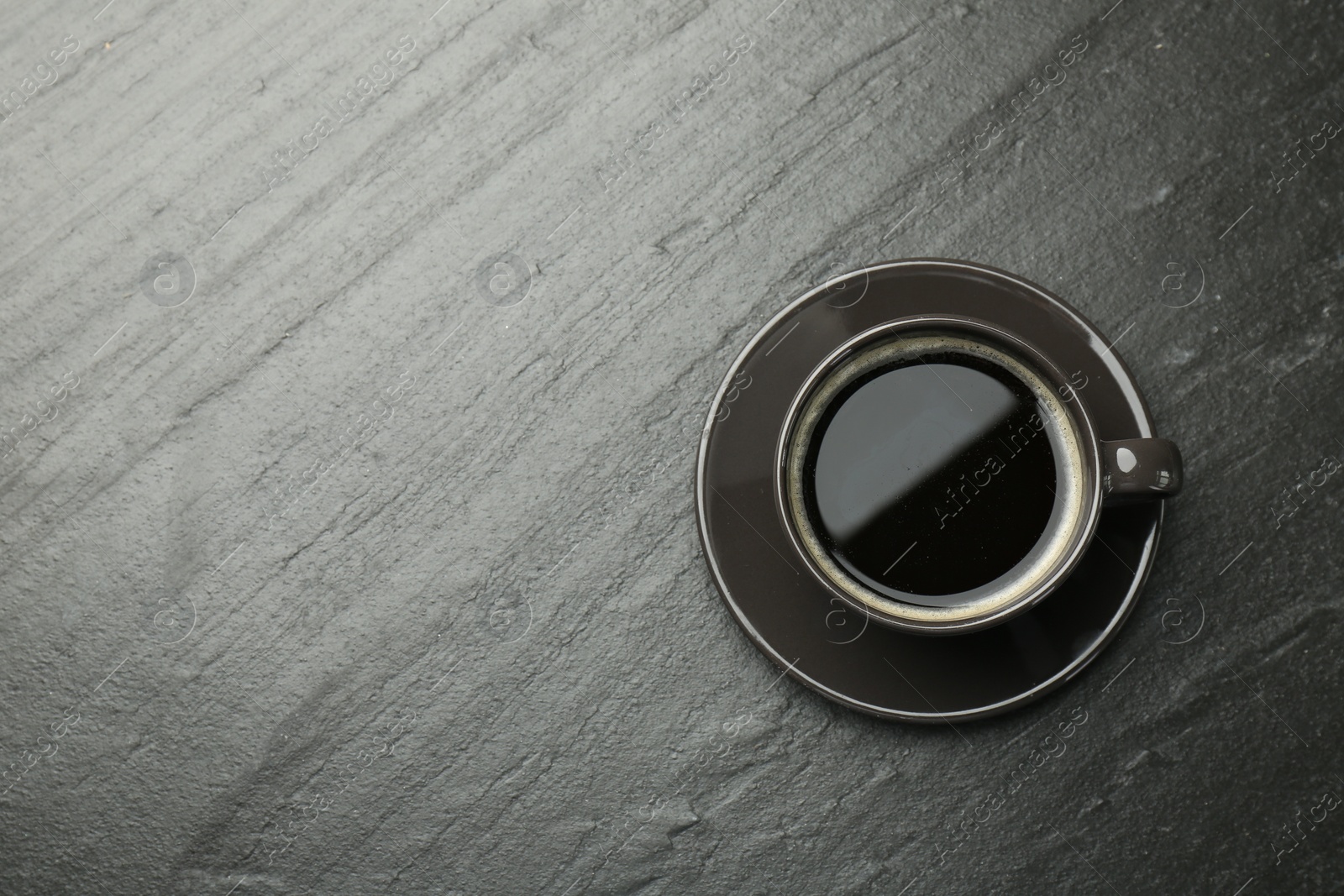 Photo of Hot coffee in cup on dark textured table, top view. Space for text