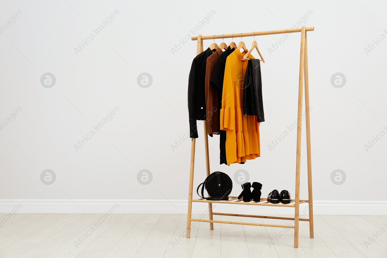 Photo of Wooden rack with stylish clothes in room. Space for text