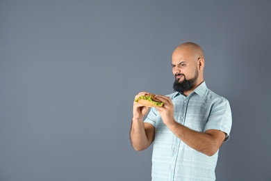 Overweight man with hamburger and space for text on gray background