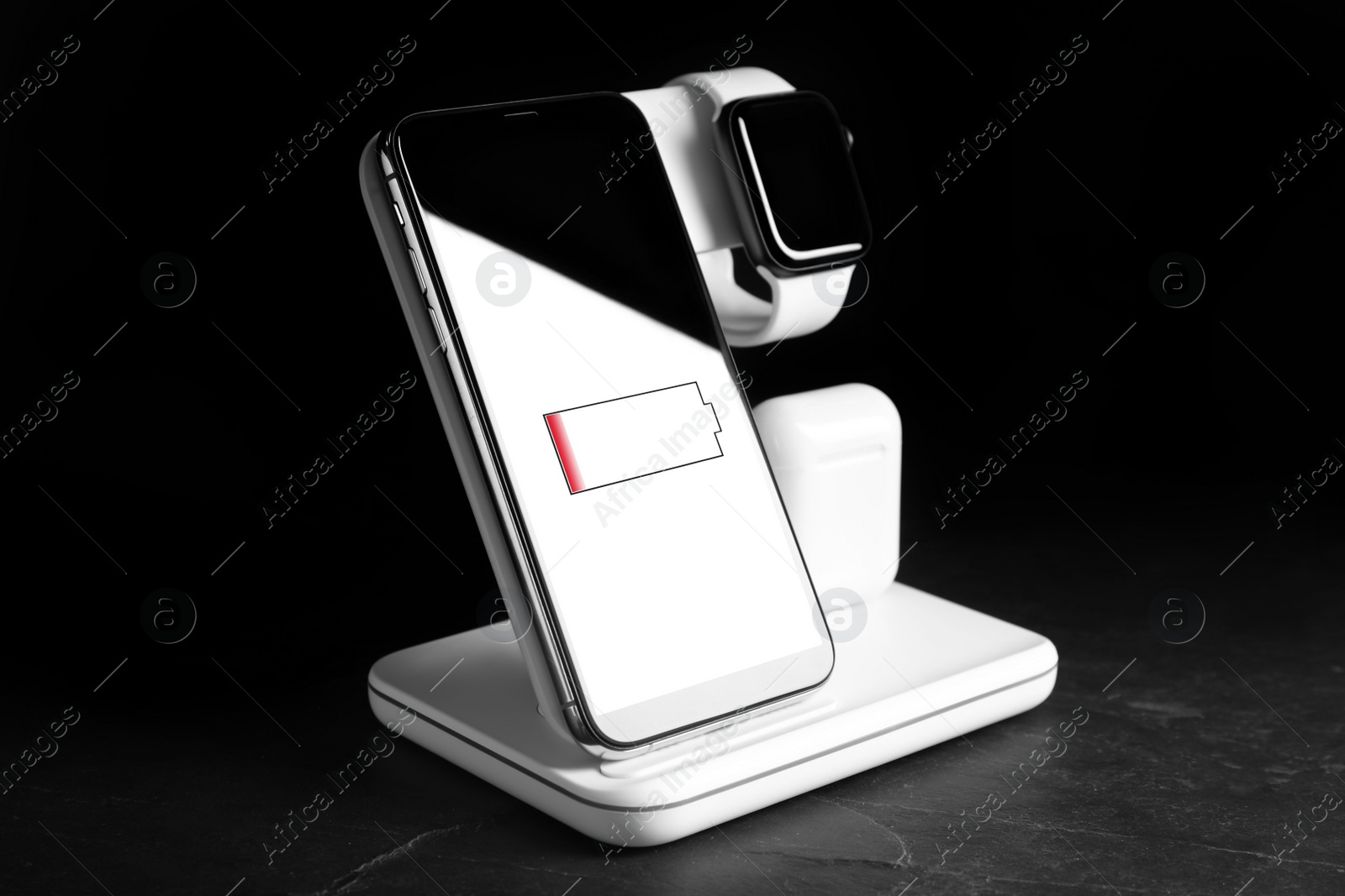 Photo of Set of gadgets charging with wireless pad on black stone table