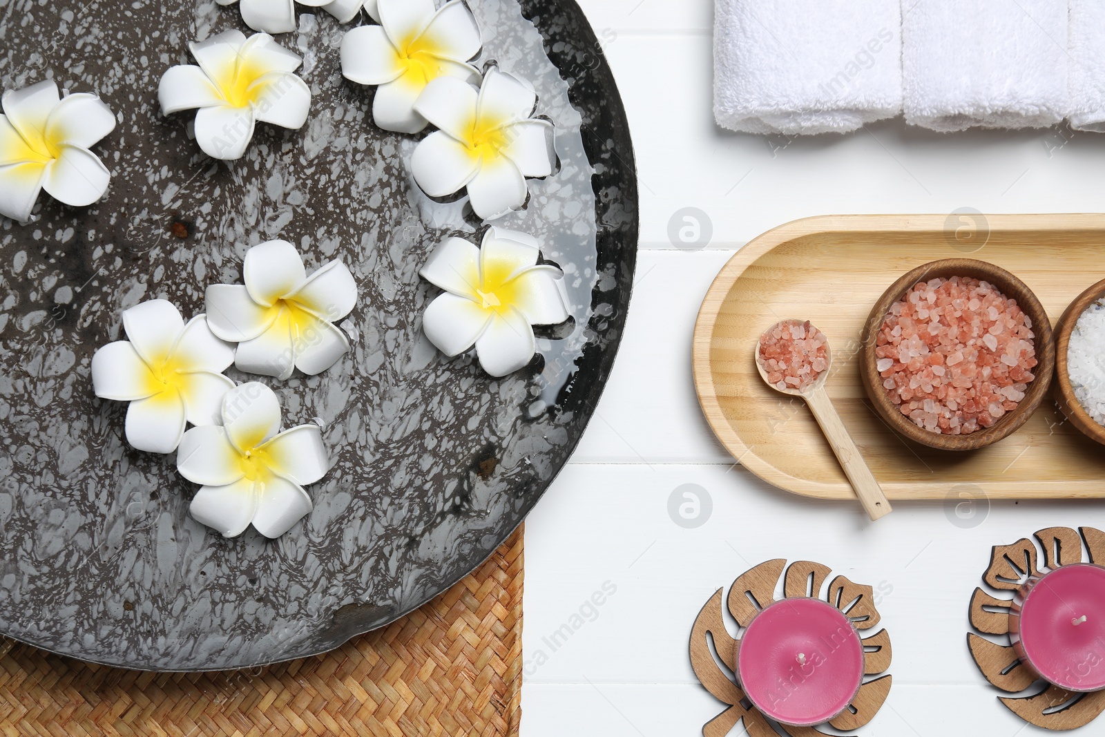 Photo of Bowl of water with flowers and different spa supplies on white wooden table, flat lay