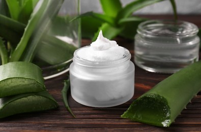 Jar of cosmetic product and cut aloe vera leaves on wooden table, closeup