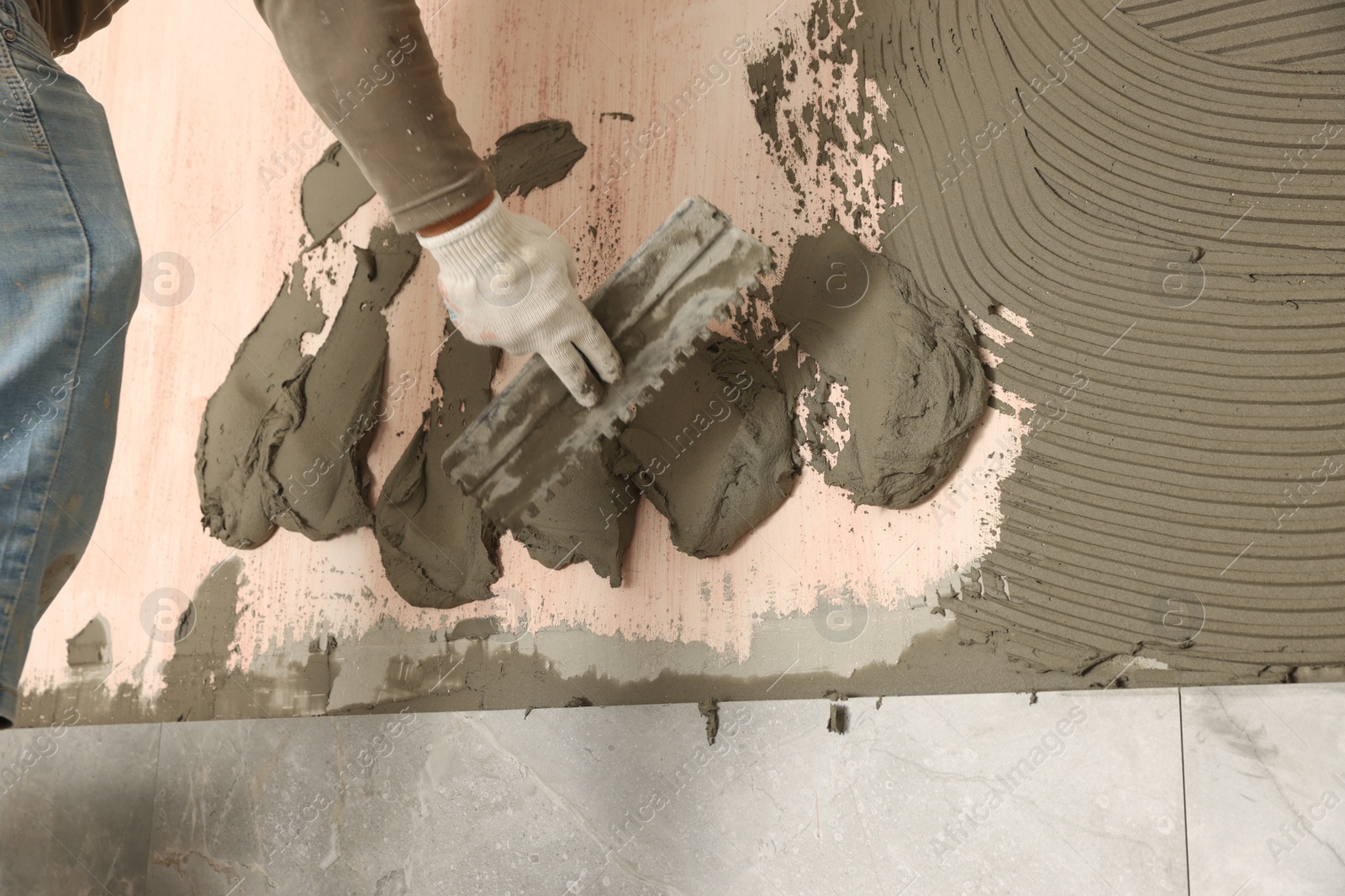 Photo of Worker applying cement on wall for tile installation, closeup