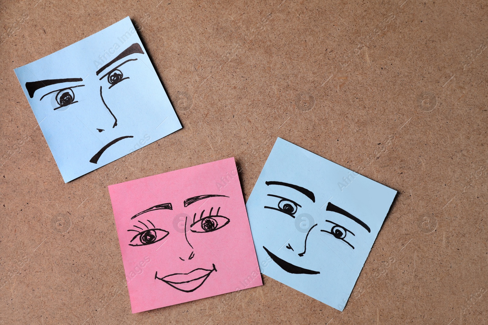 Photo of Paper notes with drawn faces on cork, flat lay. Concept of jealousy
