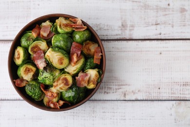 Photo of Delicious roasted Brussels sprouts and bacon in bowl on light wooden table, top view. Space for text