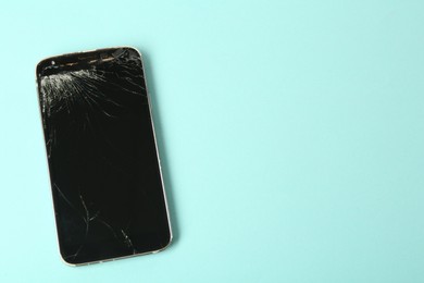 Photo of Top view of smartphone with cracked screen on light blue background, space for text. Device repair