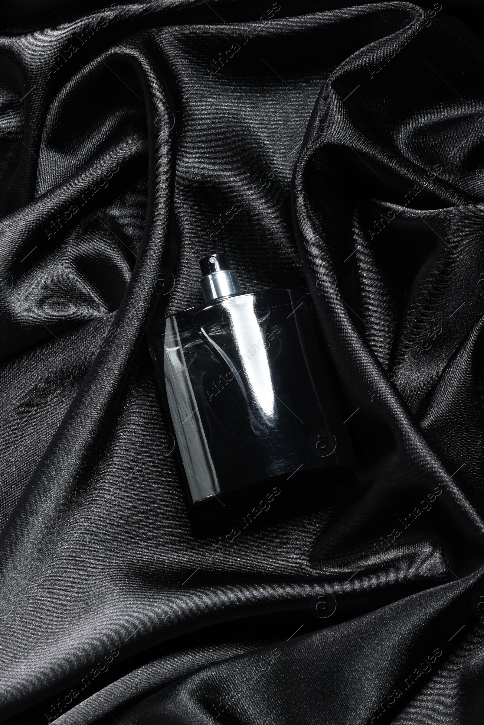 Photo of Luxury men's perfume in bottle on black satin fabric, top view