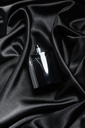Luxury men's perfume in bottle on black satin fabric, top view
