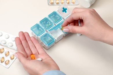 Woman taking pill from plastic container at white table, closeup