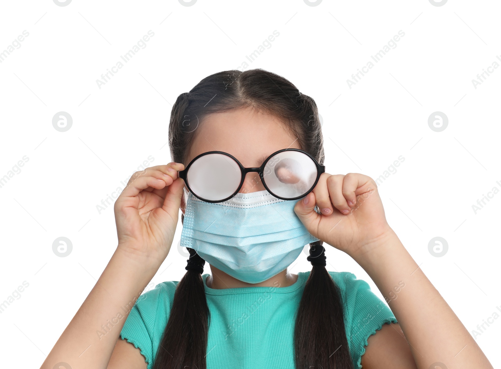 Photo of Little girl wiping foggy glasses caused by wearing medical face mask on white background. Protective measure during coronavirus pandemic