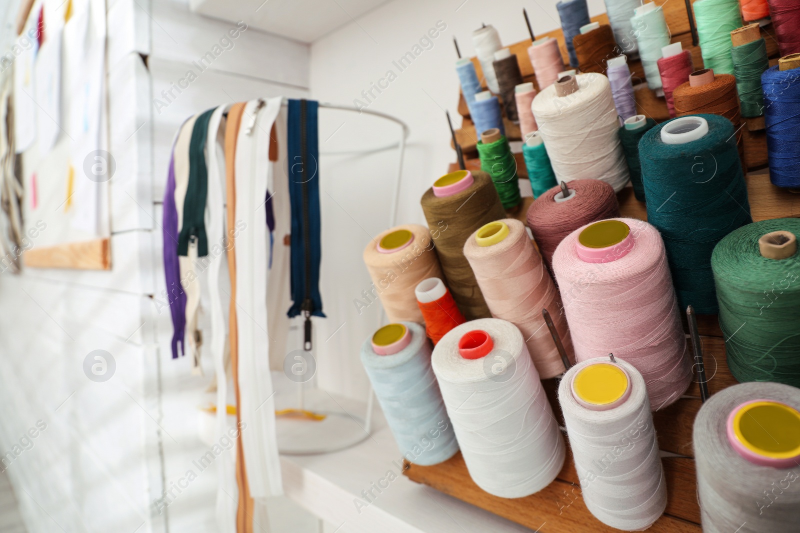 Photo of Wooden holder with collection of different threads on shelf in tailor studio