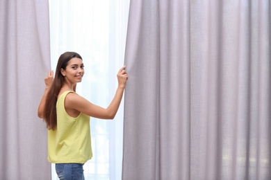 Photo of Young woman opening window curtains at home. Space for text