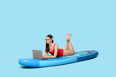 Photo of Happy woman with laptop on SUP board against light blue background