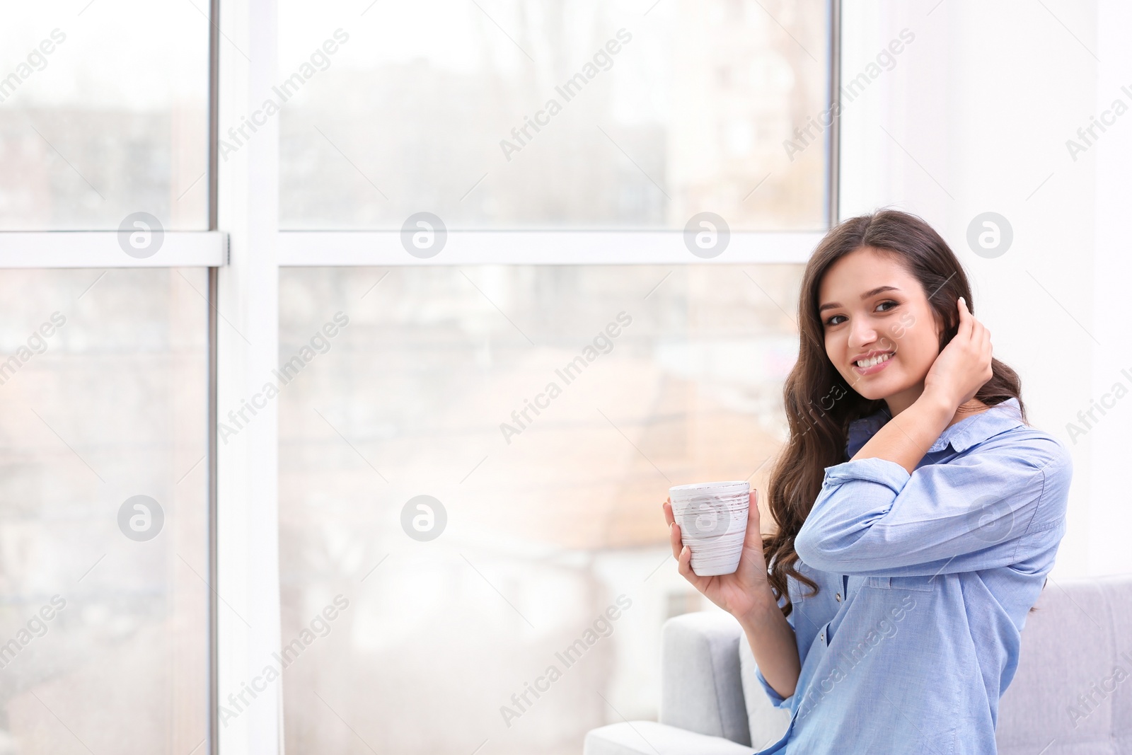 Photo of Beautiful young woman with cup of coffee near window