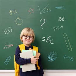 School boy holding notebooks near green chalkboard with drawings and inscriptions