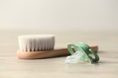 Photo of Baby pacifier and hairbrush on beige table against blurred background