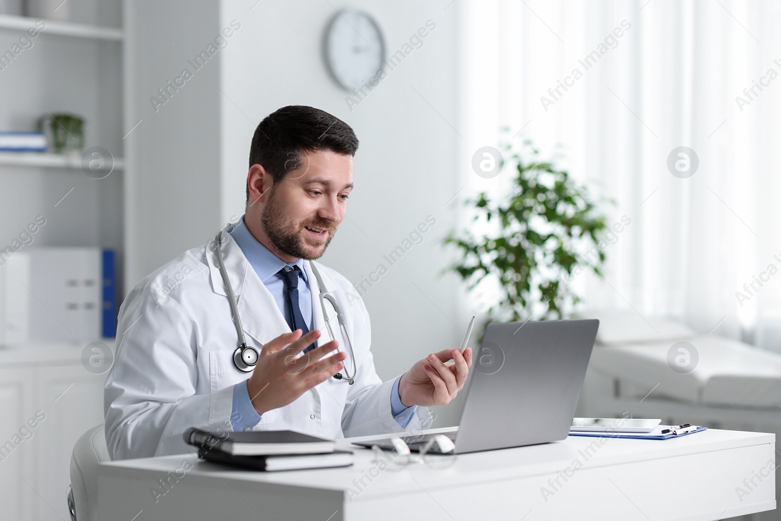 Photo of Doctor having online consultation via laptop at table in clinic