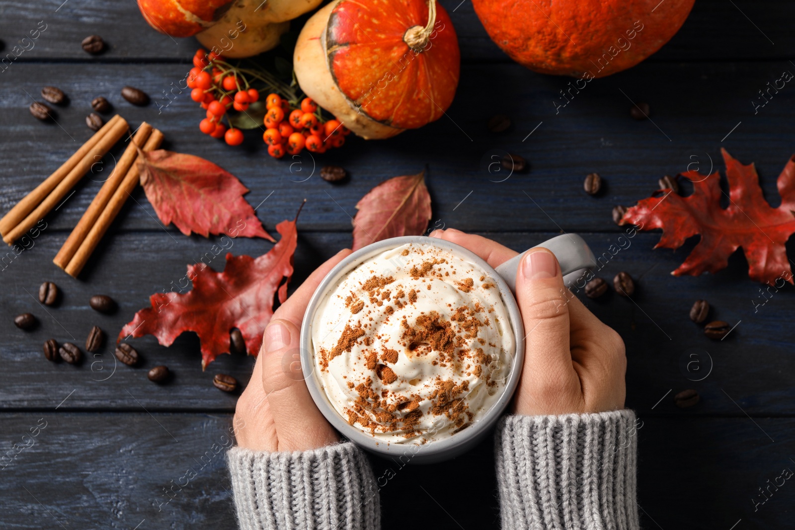 Photo of Woman with cup of tasty pumpkin spice latte at wooden table, top view