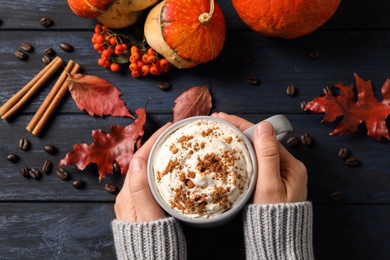 Woman with cup of tasty pumpkin spice latte at wooden table, top view