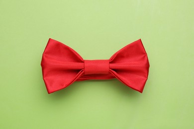 Photo of Stylish red bow tie on light green background, top view