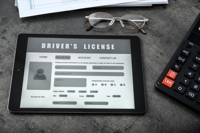 Photo of Tablet with driver's license application form, glasses and calculator on grey table