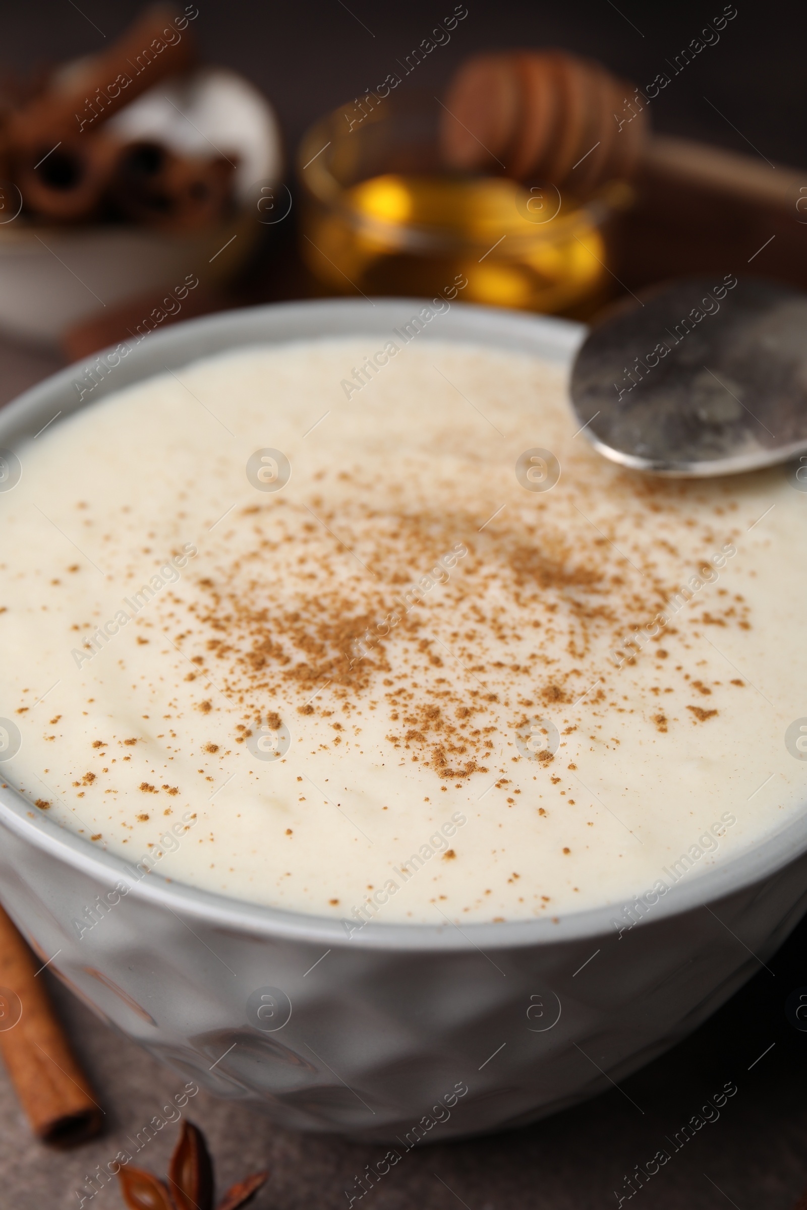 Photo of Delicious semolina pudding with cinnamon in bowl and spoon on table, closeup