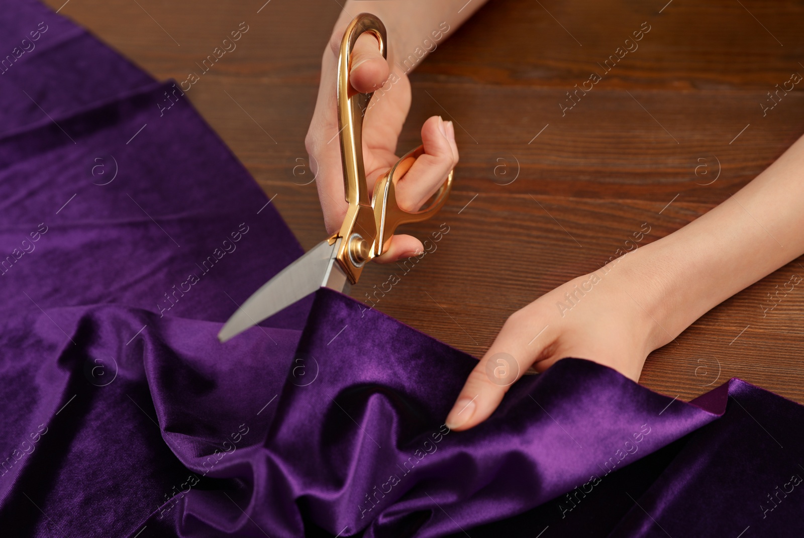Photo of Woman cutting fabric with sharp scissors at wooden table, closeup