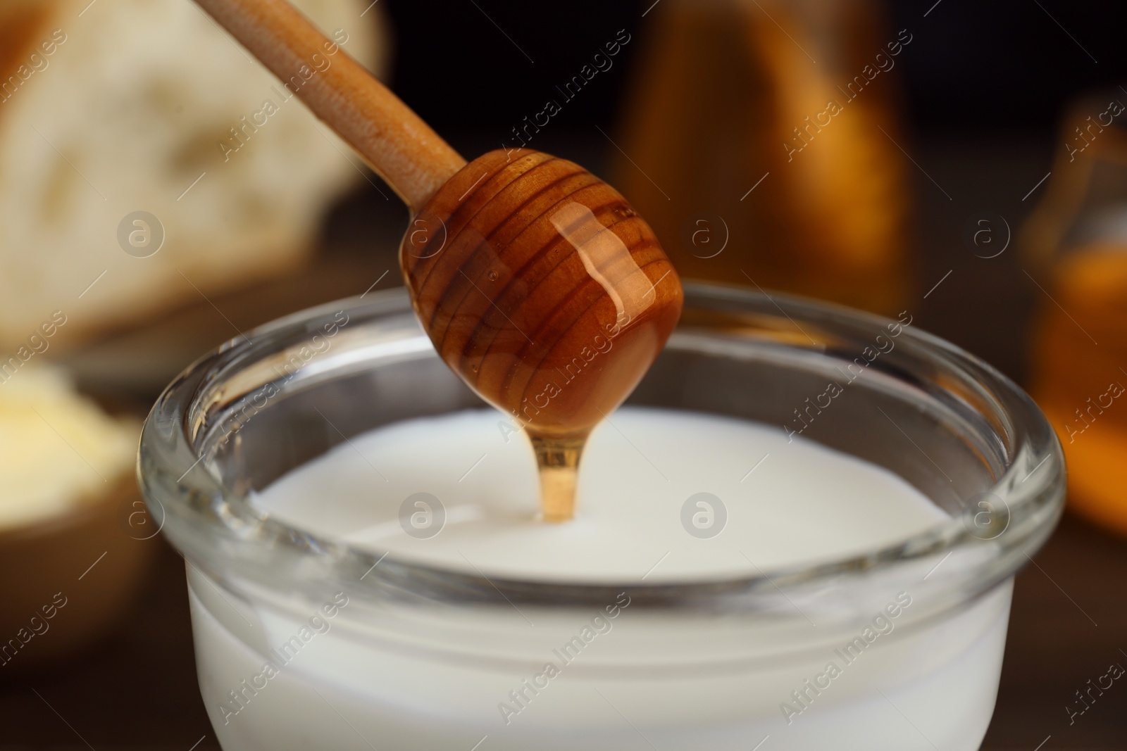 Photo of Pouring honey from dipper onto glass with milk, closeup