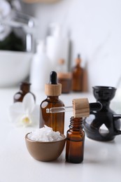 Essential oils and sea salt on white table in bathroom