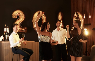 Young people celebrating New Year in club. Golden 2020 balloons on background