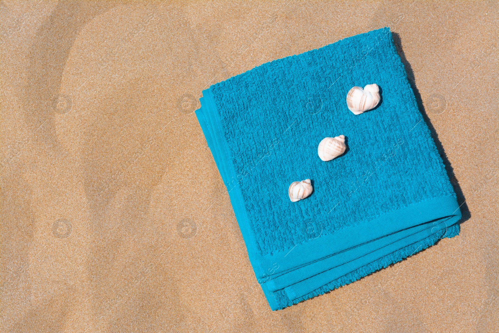 Photo of Folded soft blue beach towel with seashells on sand, flat lay. Space for text