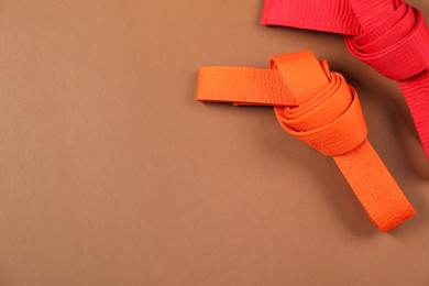 Photo of Colorful karate belts on brown background, flat lay. Space for text