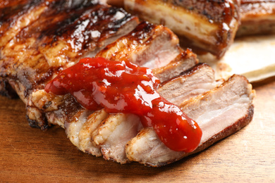 Photo of Delicious grilled ribs with sauce on wooden table, closeup
