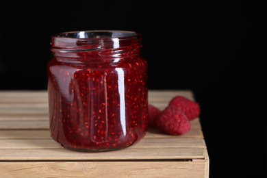 Photo of Delicious jam and fresh raspberries on wooden crate, closeup. Space for text
