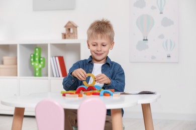 Photo of Cute little boy playing with colorful wooden pieces at white table indoors. Child's toy