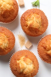 Photo of Delicious sweet muffins and brown sugar on white table, flat lay