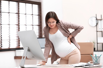 Photo of Young pregnant woman suffering from pain while working in office