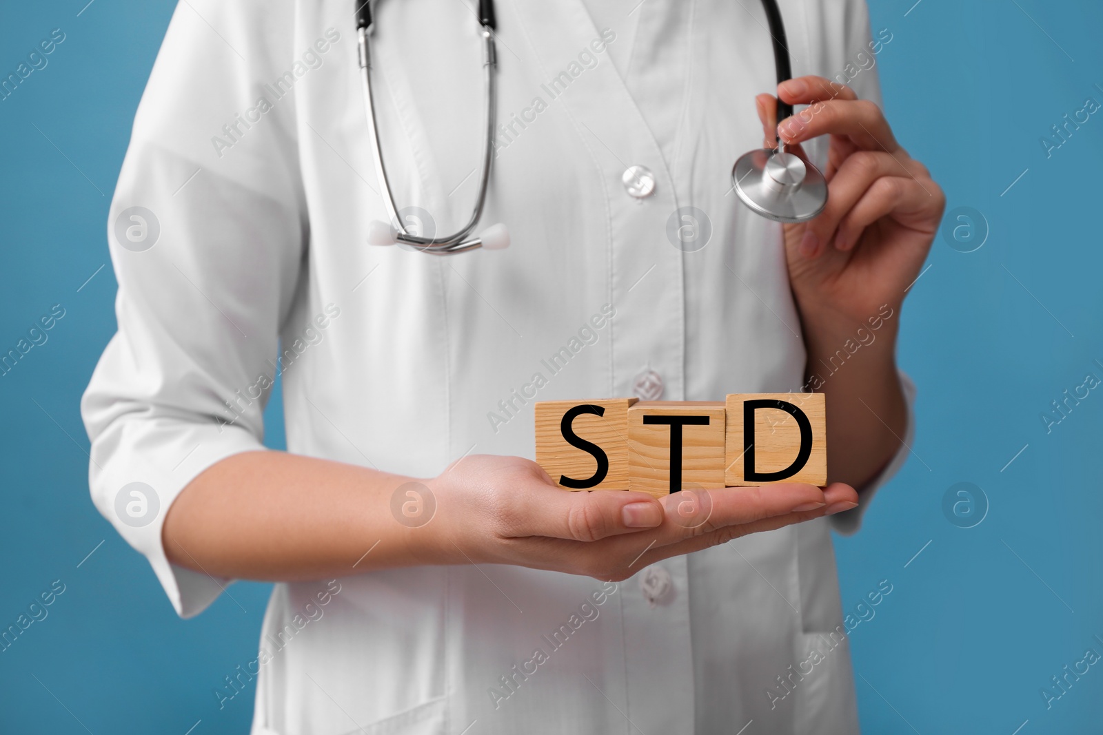 Photo of Doctor holding wooden cubes with abbreviation STD on light blue background, closeup